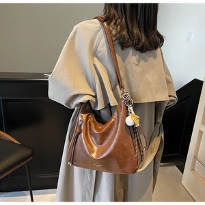 Brown leather Hobo bag detailed with tassel zipper and yellow ball charm on back of model