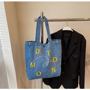Detail of light blue denim tote bag with yellow D T O M O N 3D letter embroidery and straps