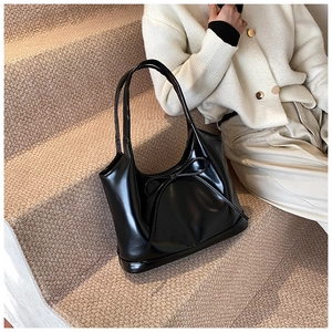 Detail of a black glossy shoulder bag with a bow knot, shown on a lifestyle background