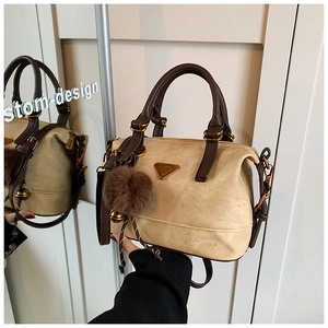 Detail of beige boston bag with brown handles, gold logo, and fluffy pompom charm