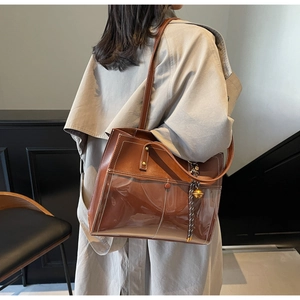 Detail of brown PU leather tote bag with transparent PVC overlay and gold bell charm