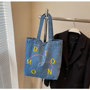 Detail view of large denim tote bag featuring yellow 3D embroidery and double straps