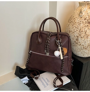Dettaglio della borsa vintage in pelle marrone con zip in metallo e ciondoli baseball