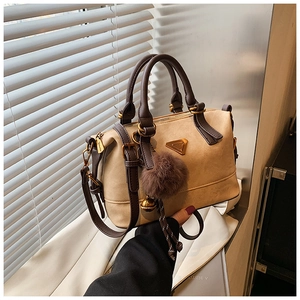 Detail of elegant beige Boston bag with golden triangular metal plaque and fluffy charm