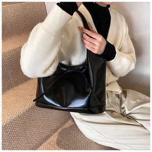 Fashionable black faux leather shoulder bag with a bow accent shown on a model