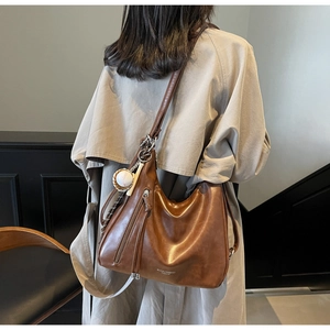 Brown faux leather crescent hobo bag with baseball charm on a trench coat model