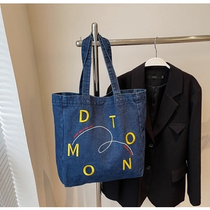 Detail of dark blue denim tote bag featuring yellow letter embroidery and white slogan