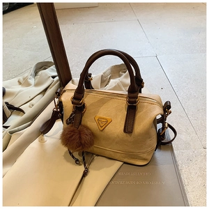 Detail view of beige suede handbag with brown leather handles and decorative fur ball charm