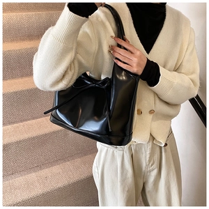 Detail of trendy black glossy underarm bag featuring a delicate bow tie on the front