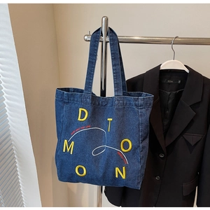 Detail of dark blue denim tote bag with yellow embroidery and red text hanging on a rack