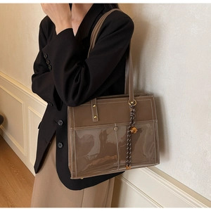 Detail of a large brown leather and transparent PVC tote bag with a woven charm