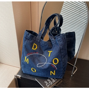 Detailed close-up of dark blue denim tote bag with yellow letters and red text embroidery