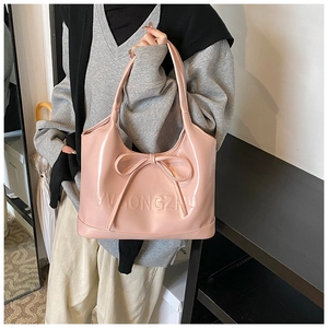 Detail of light pink patent leather tote bag featuring a large bow and embossed texture