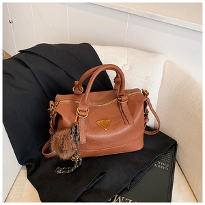 Detail of brown leather Boston bag with gold zipper and stylish fur ball charm