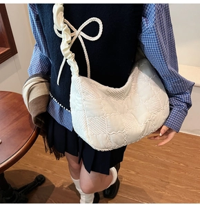 Detail of white quilted checkerboard shoulder bag with ruffled strap and bow accents