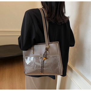 Close-up of brown leather and PVC tote bag with woven tassel and metallic bell detail