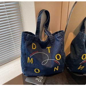 Detail of blue denim tote bag featuring yellow DTOMON embroidery and red slogan text
