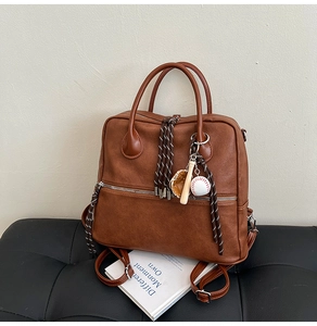 Dettaglio borsa in pelle marrone con cerniere intrecciate e ciondolo a tema baseball
