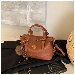 Detailed view of a brown leather boston bag with a triangle logo and plush pompom charm