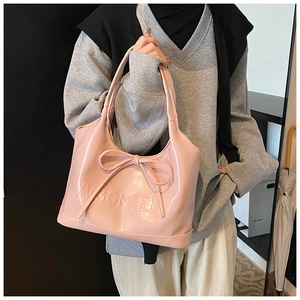 Detail of pink glossy leather handbag with bow and embossed lettering in a lifestyle setting