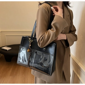 Detail of black leather tote bag with PVC pocket, contrast stitching and bell charm