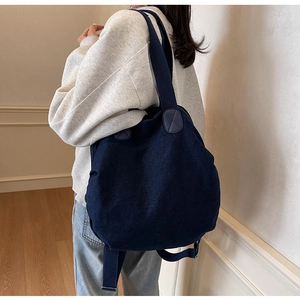 Detailed view of the back of a deep blue denim backpack worn by a model in a minimalist room
