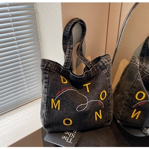 Detailed texture of washed black denim tote bag with vibrant yellow letter embroidery