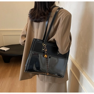 Detail of black leather and PVC tote bag with white stitching and golden bell charm