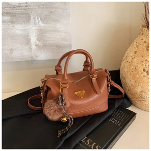 Close-up of brown litchi leather pillow bag with gold hardware and plush pom-pom charm