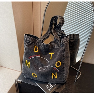 Detail of grey denim tote bag with yellow letter embroidery and white wave pattern