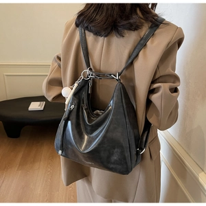 Rear view of a black shiny leather backpack with silver rings and baseball charm detail
