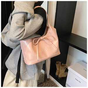 Pink faux leather tote bag with large bow detail and embossed logo shown on shoulder