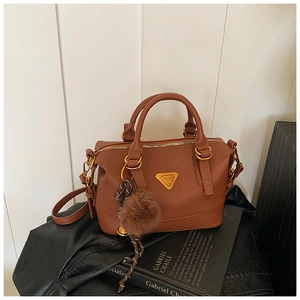 Close-up of brown pebbled leather Boston bag with golden hardware and plush ball charm