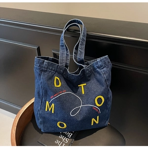 Close-up of yellow 3D embroidery and red text details on dark blue denim tote bag