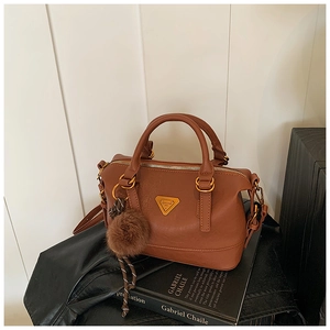 Detailed close-up of dark brown leather handbag with gold triangle plaque and fur ball charm