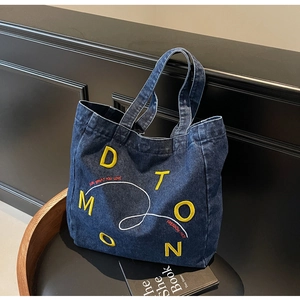 Detail of navy denim tote bag with yellow DTOMON embroidery and red slogan lettering