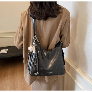 Detail of black PU leather tote bag featuring a baseball charm and branded zipper accent