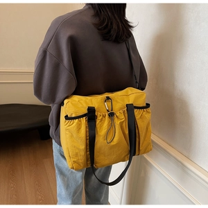 Close-up of yellow nylon tote bag side pocket with drawstring and carabiner detail