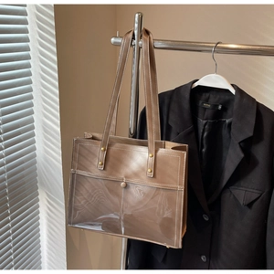 Brown leather tote bag featuring a clear PVC front pocket and gold rivet hardware accents