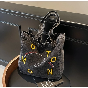 Detail of grey denim tote bag with yellow applique letters and slogan embroidery