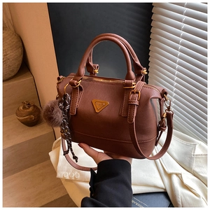 Detail of dark brown leather pillow bag with gold triangle logo and plush pendant accessory