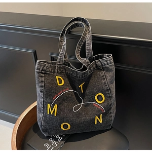 Detailed view of dark grey washed denim tote bag with yellow 3D embroidery and slogan