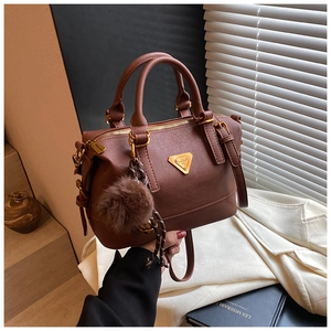 Macro shot of brown Boston bag with golden triangular plaque and faux fur pompom charm