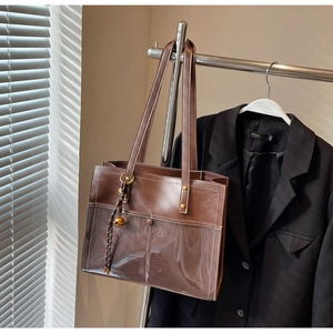 Detail of a brown tote bag with transparent PVC paneling and a golden orb charm