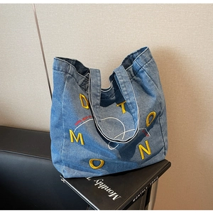 Detail of blue denim tote bag featuring yellow letter embroidery on black leather sofa