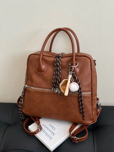 Zaino e borsa vintage in pelle marrone con ciondolo da baseball su panca in pelle nera