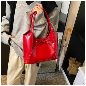 Detailed view of glossy red patent leather shoulder bag with a delicate bow ornament