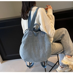 Side view of large light blue denim backpack on female model in a minimalist setting