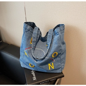 Close-up of denim tote bag featuring MOON embroidery and yellow text on black leather sofa
