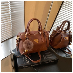 Detailed shot of brown faux leather Boston bag with gold hardware and plush pompom charm